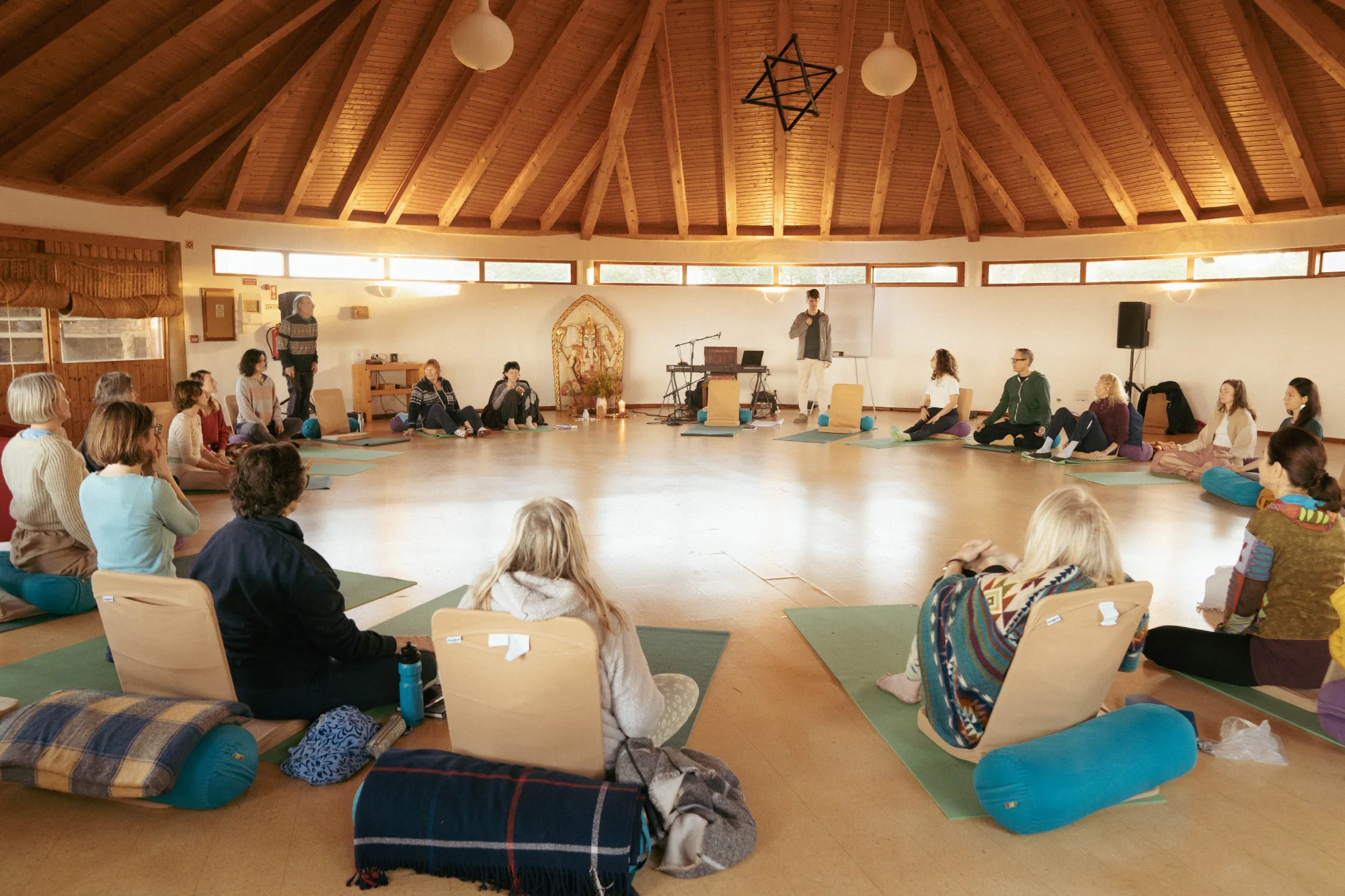 A circle of people gathered on the floor of a round retreat space, sounding together